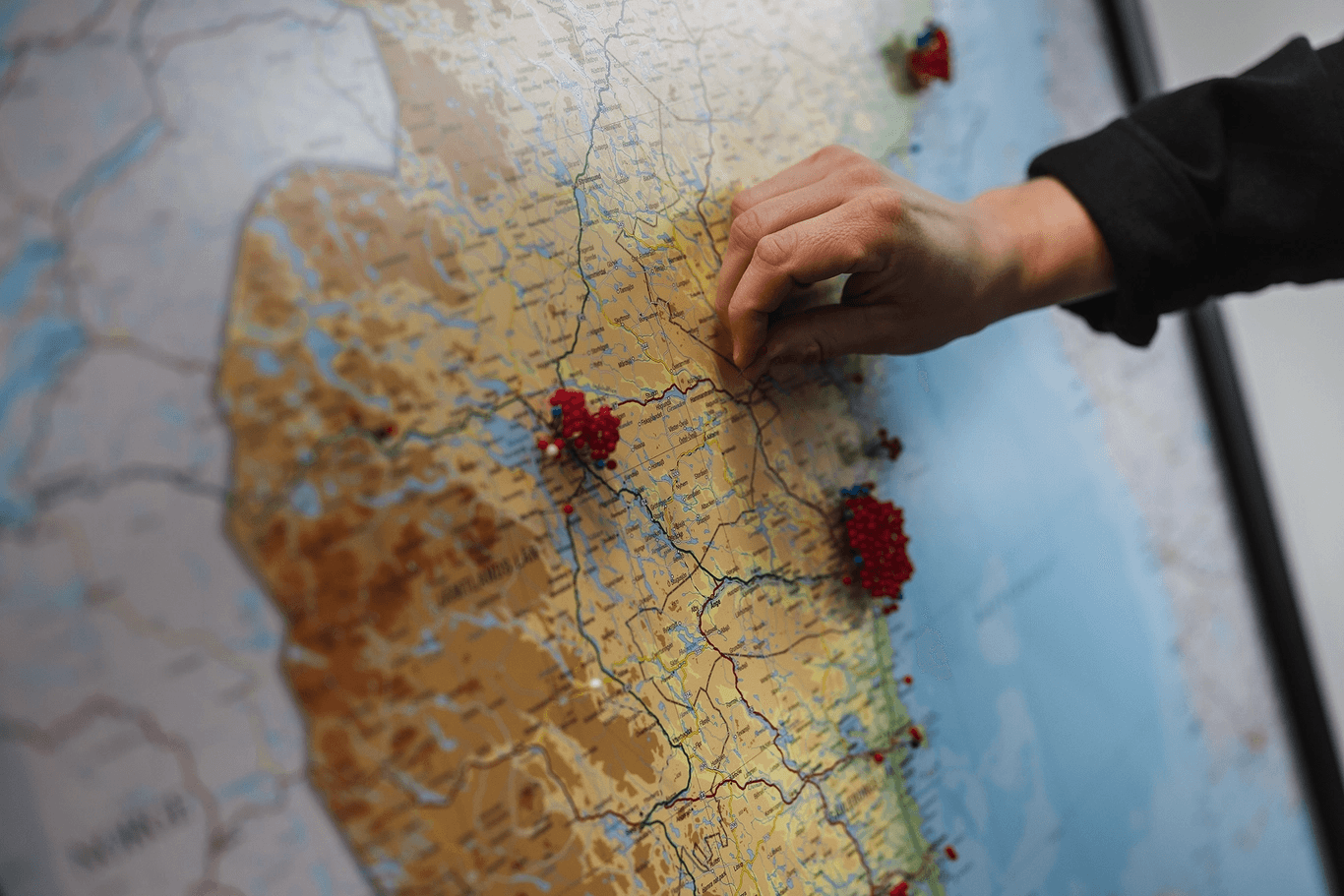 En person placerar en röd knappnål på en karta där det finns flera andra röda knappnålar som markerar platser.