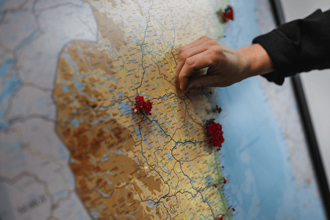 En person placerar en röd knappnål på en karta där det finns flera andra röda knappnålar som markerar platser.
