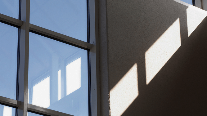 Stora fönster med solljus som kastar rektangulära skuggor på en beige innervägg.